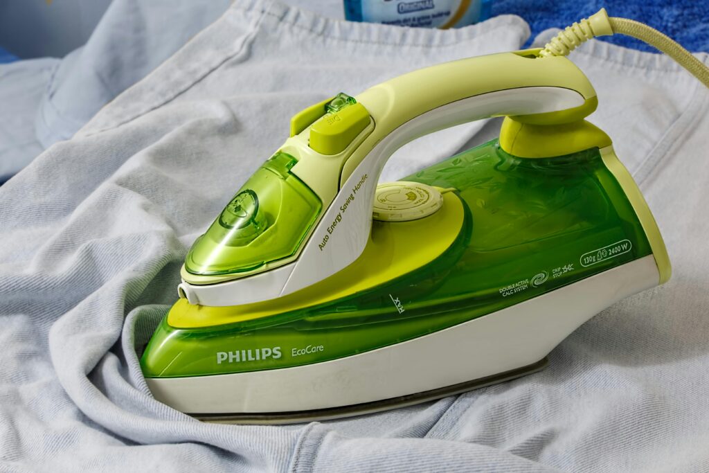 Green Philips EcoCare iron on a wrinkled shirt, ready for ironing.